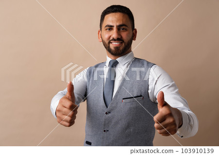 Happy young arab man showing thumbs up sign against beige background Happy young arab man showing thumbs up sign against beige background 103910139
