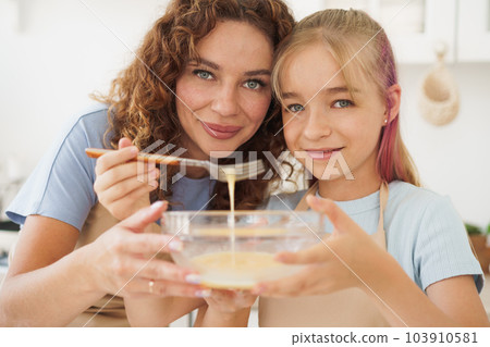 Mother and teen daughter making dough for pastry toghether in kitchen Mother and teen daughter making dough for pastry toghether in kitchen 103910581