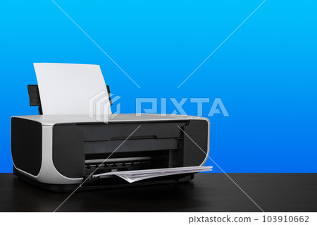 Compact laser printer on black desk against blue background 103910662