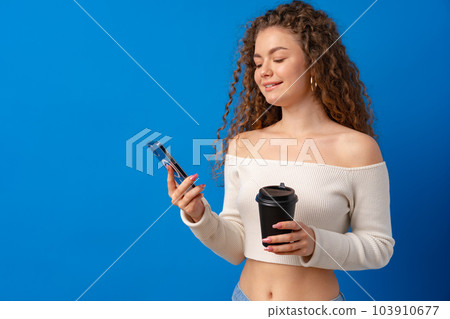Young curly woman using her smartphone against blue background Young curly woman using her smartphone against blue background 103910677
