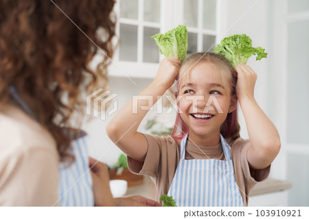 Mother and daughter playing and having fun with vegetables in kitchen 103910921