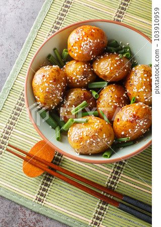 Glazed potatoes served with green onions and sesame seeds close-up in a bowl. Vertical top view Glazed potatoes served with green onions and sesame seeds close-up in a bowl. Vertical top view 103910959