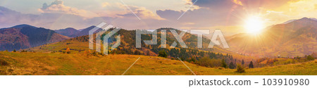 panorama of countryside landscape at sunset. grassy pasture meadows and forested hills in autumn. mountain ridge in the distance. village in the valley. clouds on the sky in evening light panorama of countryside landscape at sunset. grassy pasture meadows and forested hills in autumn. mountain ridge in the distance. village in the valley. clouds on the sky in evening light 103910980