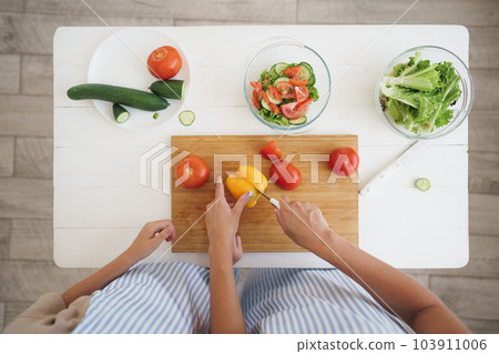 Close up of a woman and girl cutting vegetables for salad in kitchen Close up of a woman and girl cutting vegetables for salad in kitchen 103911006
