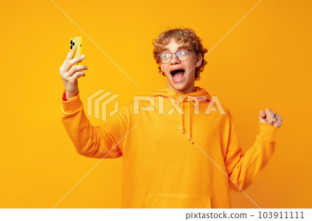 Portrait of young man playing online game on mobile phone over yellow background Portrait of young man playing online game on mobile phone over yellow background 103911111