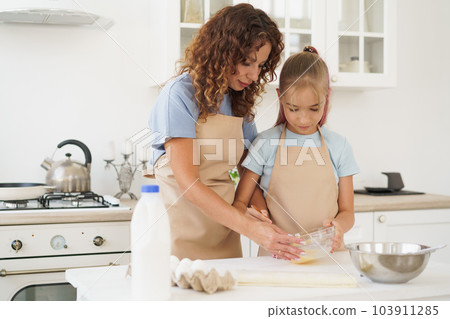 Mother and teen daughter making dough for pastry toghether in kitchen Mother and teen daughter making dough for pastry toghether in kitchen 103911285