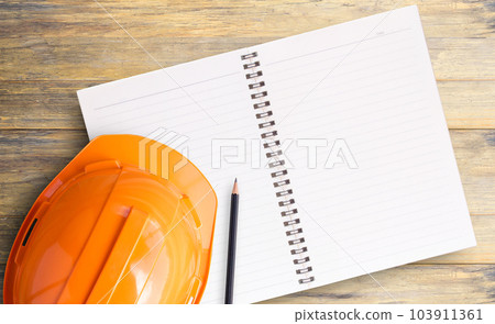 Top view with orange safety engineer helmet and notebook on wood table 103911361