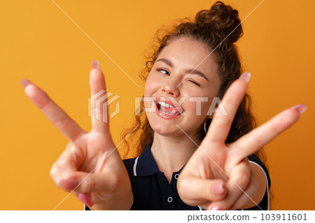 Portrait of a young funny woman showing peace gesture against yellow background 103911601