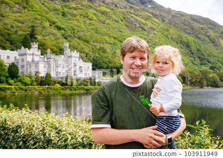 father with little daughter with Kylemore Abbey on background. Man and toddler girl. Family and small children vacations in Ireland 103911949