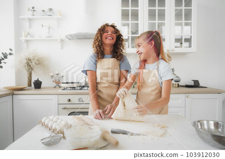 Teen girl helping her mom to cook dough in their kitchen at home 103912030