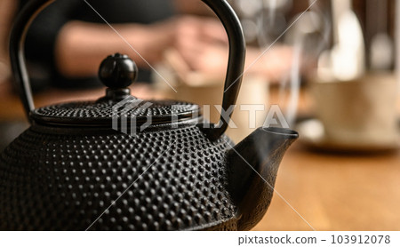 Black metal teapot with hot tea at the kitchen. Tea drinking traditions. Girl making a tea. Black metal teapot with hot tea at the kitchen. Tea drinking traditions. Girl making a tea. 103912078