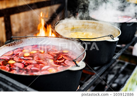 Beverages fruits and berries hot mulled wine in pots with steam in street food market. Colorful hot sweet drinks at fair festival outdoors closeup Beverages fruits and berries hot mulled wine in pots with steam in street food market. Colorful hot sweet drinks at fair festival outdoors closeup 103912886