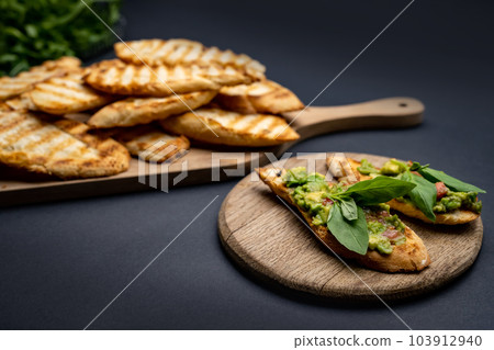 Bruschettas with toast, guacamole, basil and cherry tomatoes on wooden board. Mexican snack slice bread with avocado, herbs and vegetables Bruschettas with toast, guacamole, basil and cherry tomatoes on wooden board. Mexican snack slice bread with avocado, herbs and vegetables 103912940