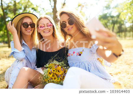 Three nice girls having fun In the park and make selfie. Excellent sunny weather. Beautiful figures. Three nice girls having fun In the park and make selfie. Excellent sunny weather. Beautiful figures. 103914403