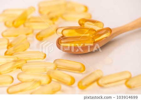 Close up of oil softgel capsules on wooden spoon with reflection. Nutritional supplement contains fish oil, omega 3, omega 6, omega 9, vitamin e, vitamin d and vitamin a. 103914699