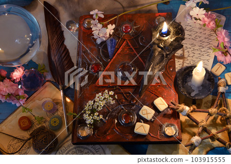 Old book of spells with runes, pentagram and candles on witch ritual table. Occult, esoteric and divination still life. Mystic background with vintage objects Old book of spells with runes, pentagram and candles on witch ritual table. Occult, esoteric and divination still life. Mystic background with vintage objects 103915555