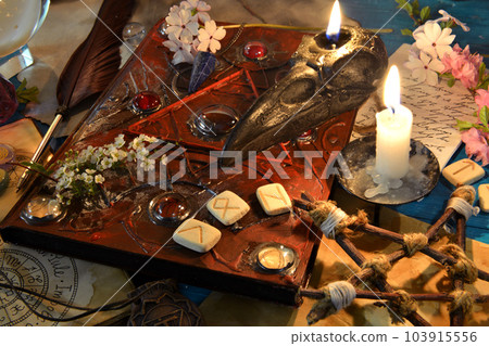 Black candle, runes and magic book of spell on witch ritual altar. Occult, esoteric and divination still life. Mystic background with vintage objects Black candle, runes and magic book of spell on witch ritual altar. Occult, esoteric and divination still life. Mystic background with vintage objects 103915556