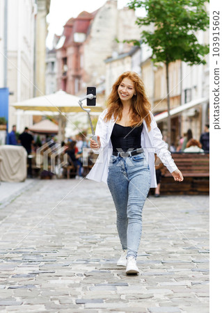 Young redheaded beautiful woman walking and using her mobile phone Young redheaded beautiful woman walking and using her mobile phone 103915602