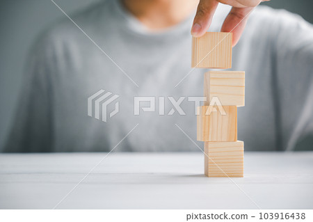 Abstract concept of growing success. Hand holding and stacking blank wooden blocks, symbolizing the steps of business growth and success. Copy space for text or graphics. Brown wooden blocks against 103916438