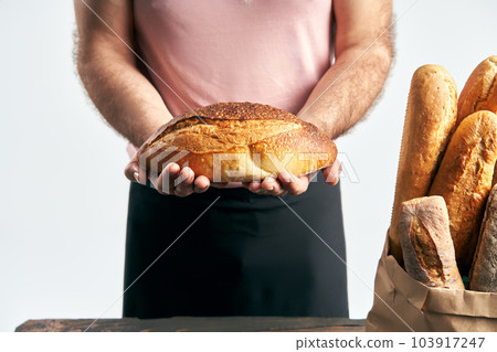 Baker man in apron holding loaf of fresh baked bread in the hands Baker man in apron holding loaf of fresh baked bread in the hands 103917247