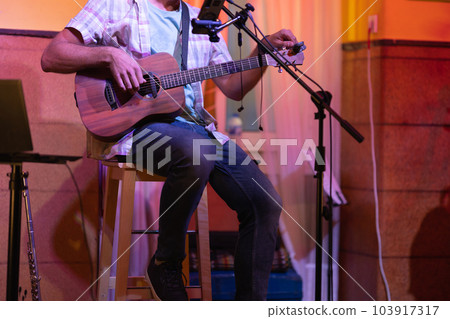 Man sitting on stage with an ukulele Man sitting on stage with an ukulele 103917317