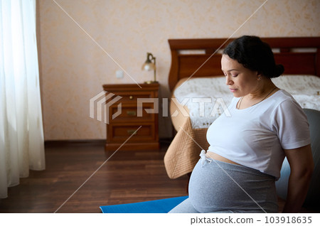 Portrait of middle-aged pregnant woman with a big belly in the third trimester of pregnancy, exercising at home on a yoga mat. Expecting a child. Pregnancy. Motherhood and maternity lifestyle concept 103918635