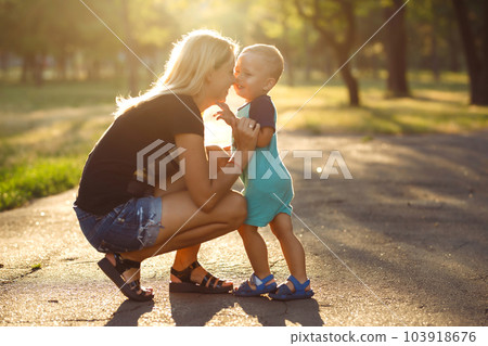 Kiss and hugs of mom and son. Mom and son walk in the summer park. Family holiday and togetherness. Kiss and hugs of mom and son. Mom and son walk in the summer park. Family holiday and togetherness. 103918676
