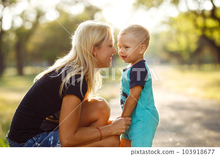 Kiss and hugs of mom and son. Mom and son walk in the summer park. Family holiday and togetherness. Kiss and hugs of mom and son. Mom and son walk in the summer park. Family holiday and togetherness. 103918677