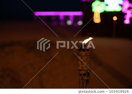 A burning torch at night on the beach against the backdrop of a bar close-up. A burning torch at night on the beach against the backdrop of a bar close-up. 103919926