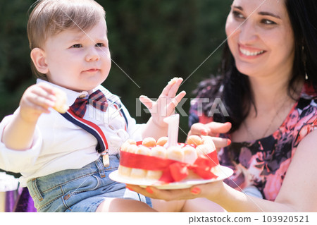 Festive family gathering - A beaming baby boy is joined by his mother as they commemorate his special day with a birthday cake adorned with a lone candle. Festive family gathering - A beaming baby boy is joined by his mother as they commemorate his special day with a birthday cake adorned with a lone candle. 103920521