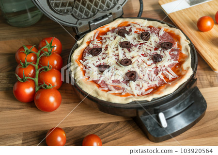 Homemade pizza waffle with pepperoni, olives and parmesan cheese ready to bake in a waffle iron 103920564