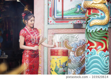 Chinese woman in a red cheongsam dress holding incense pay homage to Chinese god at shrine. Concept to celebrate Chinese New Year. 103920614
