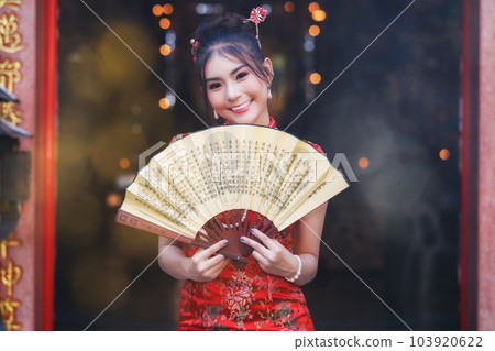 Chinese woman in a red cheongsam dress holding fan at shrine. Concept to celebrate Chinese New Year. Chinese woman in a red cheongsam dress holding fan at shrine. Concept to celebrate Chinese New Year. 103920622