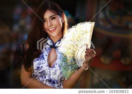 Chinese woman in cheongsam dress holding fan at shrine. Concept to celebrate Chinese New Year. 103920651