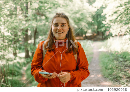 Happy beautiful woman listening music on headphones in the nature in the forest, carrying a backpack in the forest on sunset light in the summer season. Happy beautiful woman listening music on headphones in the nature in the forest, carrying a backpack in the forest on sunset light in the summer season. 103920938