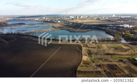 Urban beautiful landscape agricultural plowed fields, lakes for growing fish, gardens, plants,building industrial area of city, cloud shadows on sunny autumn day. Aerial drone view. Urban beautiful landscape agricultural plowed fields, lakes for growing fish, gardens, plants,building industrial area of city, cloud shadows on sunny autumn day. Aerial drone view. 103921382