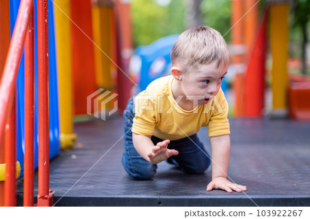 Curious preschooler with Down syndrome sitting on colorful climber at modern playground in residential complex blond kid enjoying outdoor activities in city Curious preschooler with Down syndrome sitting on colorful climber at modern playground in residential complex blond kid enjoying outdoor activities in city 103922267