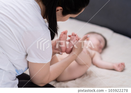Caring mother holding tender bare feet of baby with hands sitting on soft bed brunette woman showing love and care for little boy at home after waking up in morning Caring mother holding tender bare feet of baby with hands sitting on soft bed brunette woman showing love and care for little boy at home after waking up in morning 103922278