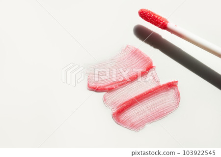 Smears of shining lip gloss and lip gloss brush on white background, hard shadows 103922545