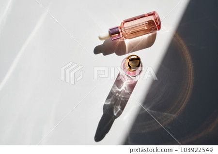 Cosmetic product bottles with rose petals and hard shadow. Skincare beauty product concept Cosmetic product bottles with rose petals and hard shadow. Skincare beauty product concept 103922549