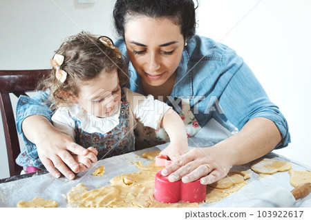 Mother and daughter baking cookies in the kitchen - cutting pastry dough with plastic shape cutters 103922617
