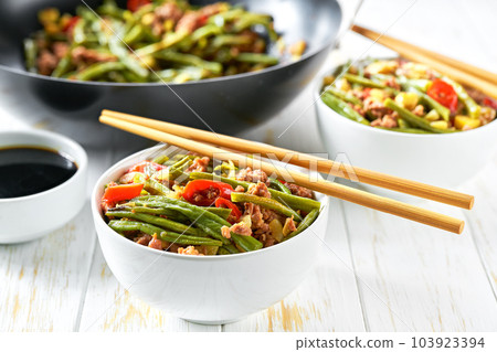Spicy chinese sichuan stir-fried green beans in a wok with  garlic, red pepper and ginger, on a wooden table. 103923394