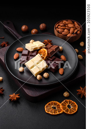 A mix of several types of delicious sweet chocolate broken into cubes on a black plate A mix of several types of delicious sweet chocolate broken into cubes on a black plate 103923508