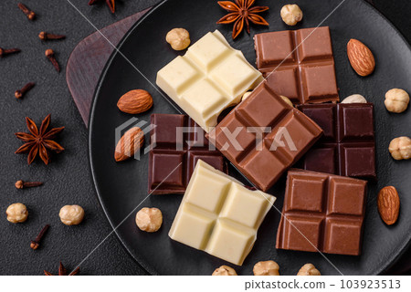 A mix of several types of delicious sweet chocolate broken into cubes on a black plate A mix of several types of delicious sweet chocolate broken into cubes on a black plate 103923513