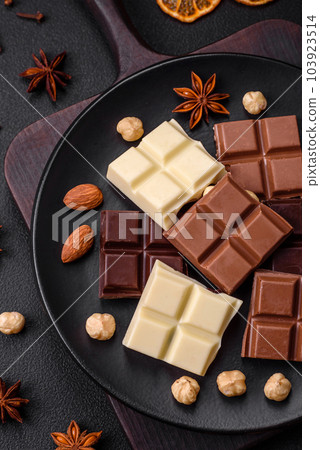 A mix of several types of delicious sweet chocolate broken into cubes on a black plate A mix of several types of delicious sweet chocolate broken into cubes on a black plate 103923514