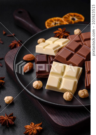 A mix of several types of delicious sweet chocolate broken into cubes on a black plate A mix of several types of delicious sweet chocolate broken into cubes on a black plate 103923515