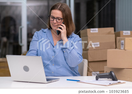 woman using laptop and phone to check product orders and save data while running her online business from a storehouse using express shipping services woman using laptop and phone to check product orders and save data while running her online business from a storehouse using express shipping services 103923685