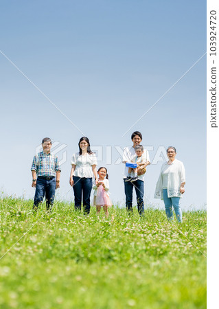 A three-generation family standing on a blue sky hill 103924720