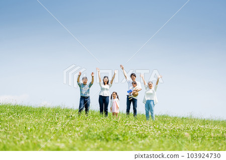 A three-generation family standing on a blue sky hill 103924730