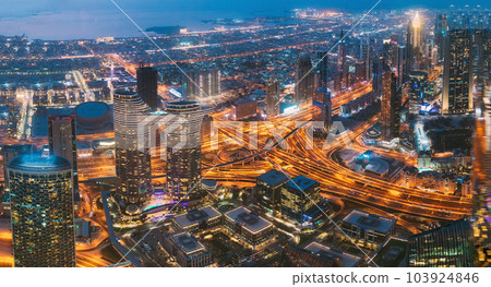 Aerial View Of Evening Night Scenic View Of Skyscraper In Dubai. Street Night Traffic In Dudai Skyline. Waterfront And Dubai Cityscape In Summer Evening Illuminations. Urban background. High quality Aerial View Of Evening Night Scenic View Of Skyscraper In Dubai. Street Night Traffic In Dudai Skyline. Waterfront And Dubai Cityscape In Summer Evening Illuminations. Urban background. High quality 103924846